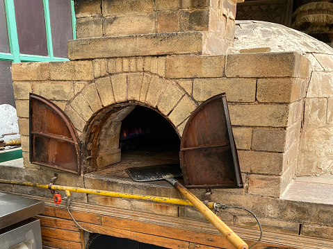 Stock photo showing close-up view of long handled metal pizza paddle shovel in traditional wood burning brick pizza oven.