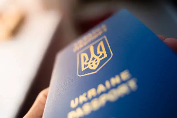 Photo of Ukrainian biometric passport in hand close-up on a blurred background. Coat of arms of Ukraine in the form of a trident. Blue document proof of identity and citizenship of a Ukrainian