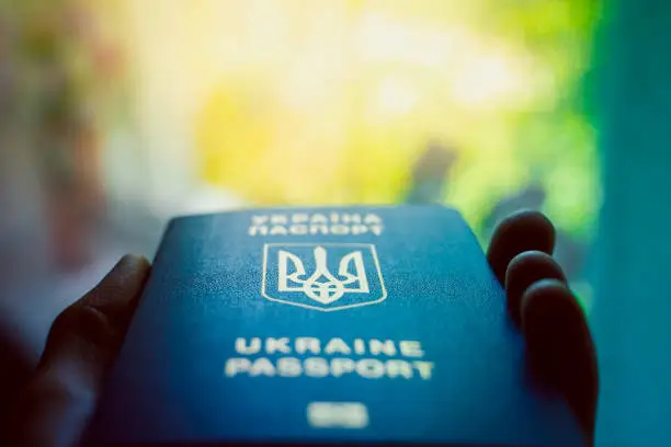 Photo of Ukrainian biometric passport in hand close-up on a blurred background. Coat of arms of Ukraine in the form of a trident. Blue document proof of identity and citizenship of a Ukrainian