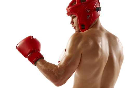 Punch. Young muscled athlete, professional kickboxer in protective helmet and boxing gloves in action isolated on white background. MMA, sport, competition, energy, combat sports.