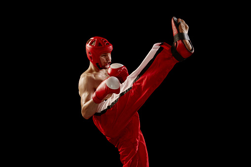 Champion. Studio shot of male kickboxer, mma fighter in motion and action isolated over dark background. Muay thai. Sport, competition, energy, combat sports. Red and black