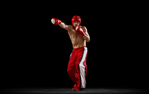 Champion. Studio shot of male kickboxer, mma fighter in motion and action isolated over dark background. Muay thai. Sport, competition, energy, combat sports. Red and black