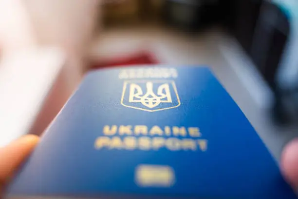 Photo of Ukrainian biometric passport in hand close-up on a blurred background. Coat of arms of Ukraine in the form of a trident. Blue document proof of identity and citizenship of a Ukrainian