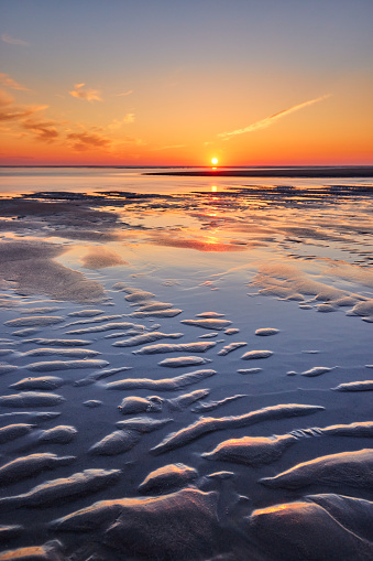 Sunset over dutch sea. The sun is about to set and the position of the water has all left behind structures in which the sun reflects