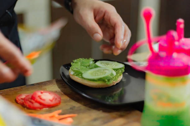 Chef puts tomato slice for burger filling, on kitchen utensils background. stock photo