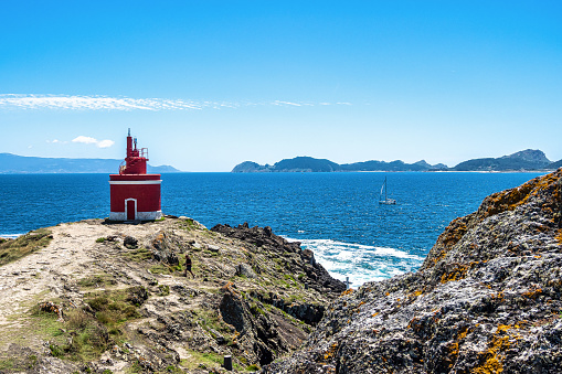 Red lighthouse in Punta Robaleira, Costa da Vela, Pontevedra, Galicia, Spain. With the Cies Islands in the background