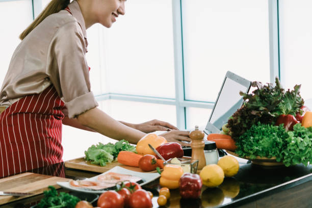 istock Asian woman cooks Viewing recipes from the internet using a laptop computer on a modern kitchen counter full of fresh vegetables. 1443264362