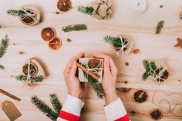 istock Eco-friendly Christmas gift packaging, zero-waste, no plastic holidays. Female hands holding handmade craft gift box decorated with spruce, cinnamon and dried orange. Top view, selective focus. 1443267771