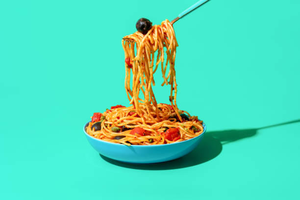 istock Eating spaghetti puttanesca from a bowl, minimalist on a green background 1443274893