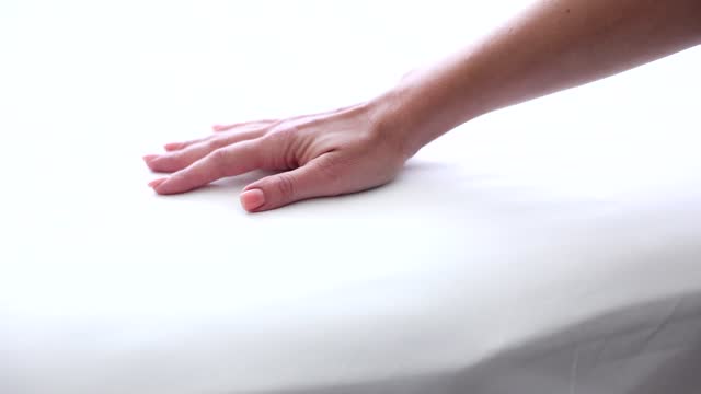 Female hand testing hardness of white orthopedic mattress