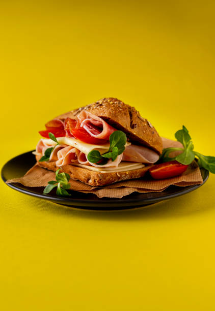 A close-up of a toasted sandwich, cut in half diagonally and served on a plate. The bread is golden brown and toasted, and the filling appears to be ham and possibly cheese and lettuce or other greens. The image focuses on the texture of the bread and the presentation of the sandwich, suitable for food photography and menu illustrations.