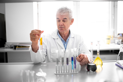 Older male scientist seen working on an experiment in a laboratory using pipette and test tubes during some biochemical research.