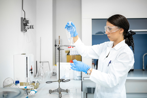 Brown haired female scientist seen working on an experiment in a laboratory using pipette and test tubes during some research.