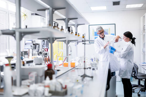 Two colleagues seen in a research lab working with some medical bottles Two laboratory technologists seen working with some medical bottles, tubes and pipettes during an experiment. chemistry lab pictures stock pictures, royalty-free photos & images