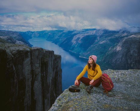Young Caucasian woman sitting on Preikestolen and looking at view