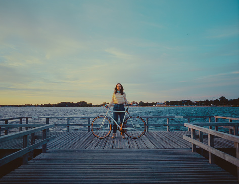 Young Caucasian woman with bicycle near the lake at sunset. Shot on film