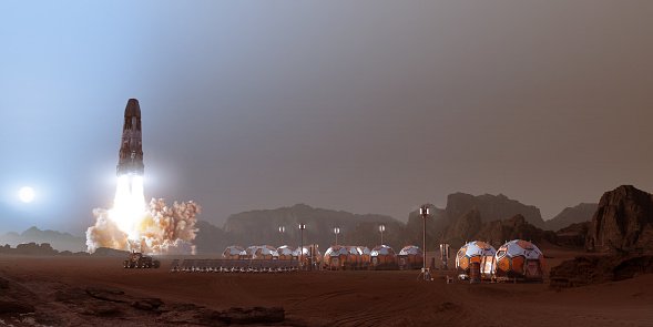A rocket taking off from the surface of Mars, viewed from a small base camp consisting of co-joined pods with solar panes, lights and a Mars rover. It's dusk and the sun is setting - Sunsets on Mars are blue.