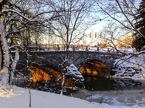 Winter landscape with  Helsinki - Vantaa frontier sign on the stone bridge over the frozen river with sunlighted arched and trees around