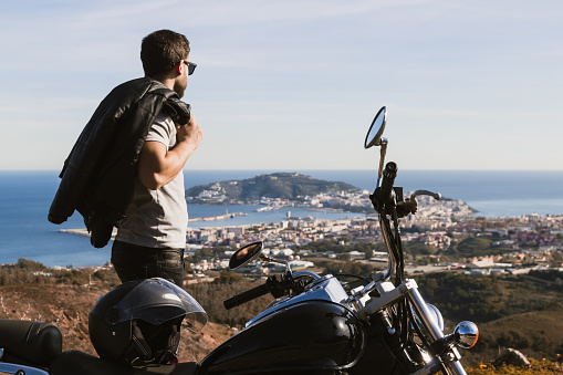 Biker with sunglasses and leather jacket on his shoulder looking at the horizon