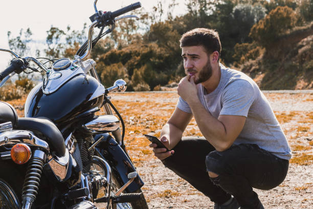 Crouching biker worried about a motorcycle breakdown Crouching biker worried about a motorcycle breakdown engine failure stock pictures, royalty-free photos & images