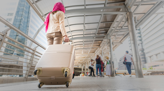 Muslim traveler woman walking and carrying a suitcase in a travel location on holidays or business trip, traveling concepts, Rear view .
