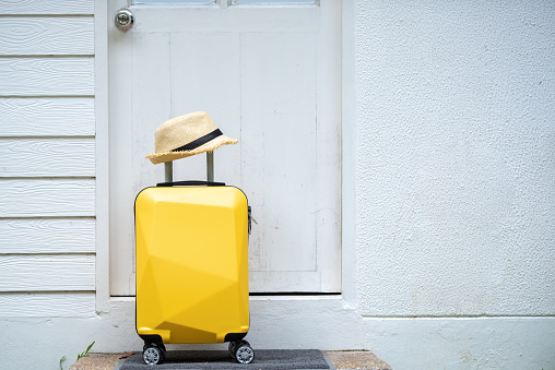 Yellow suitcase, luggage with hat at front door, Leaving home for a holiday and vacation, travel, get ready for adventure.