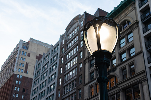 A glowing street light on during the evening in front of a row of old skyscrapers in the Flatiron District of New York City