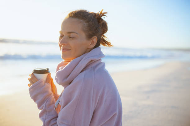 smiling elegant woman in cosy sweater at beach in evening stock photo