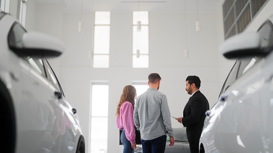 A car salesman is showing new cars to a couple.