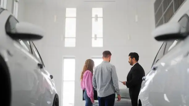 Photo of Car salesman showing new cars to couple