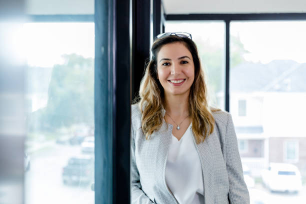 Female administrator leans against office wall and smiles for camera