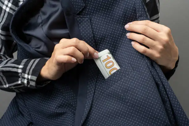 a woman takes out or puts one hundred Dollar cash money in nominal 100 USD from an elegant jacket pocket. Close up