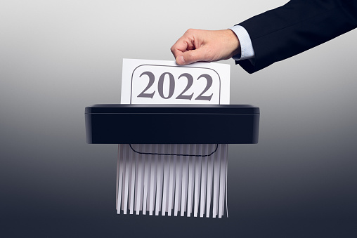 The end of the year 2022. The hand of a man wearing a suit pushes 2022 documents or calendar into a paper shredder.