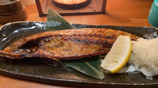 A plate of Japanese seafood consisting of a grilled pacific herring with lemon and radish. Served at a Japanese robatayaki restaurant, where food is cooked on a grill in front of customers.