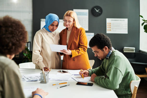 istock Mature blond teacher showing document with test to Muslim female student 1443305405