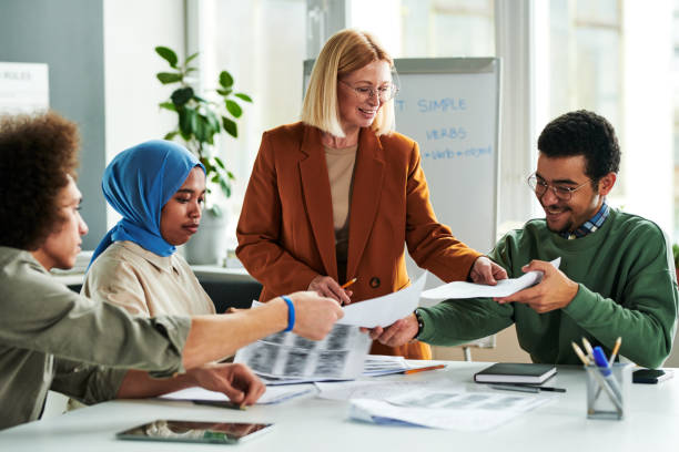 Happy mature teacher passing papers with grammar test or authentic materials