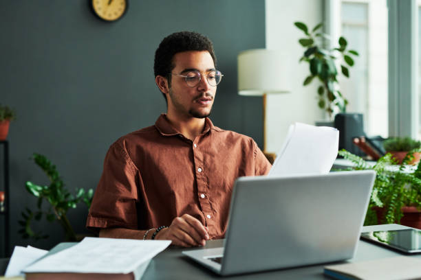 istock Young confident man with papers sitting in front of laptop 1443305514