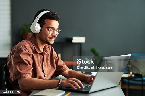 istock Young smiling man in headphones typing on laptop keyboard 1443305526