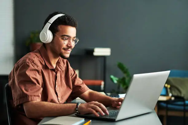 Photo of Young smiling man in headphones typing on laptop keyboard
