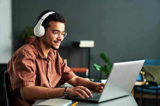 young smiling man in headphones typing on laptop keyboard - deduction imagens e fotografias de stock