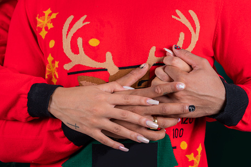 Afro-Latin couple of average age between 25 and 30 years old are inside a photographic studio dressed in red Christmas jackets and a green background, embracing each other, they show their hands clasped
