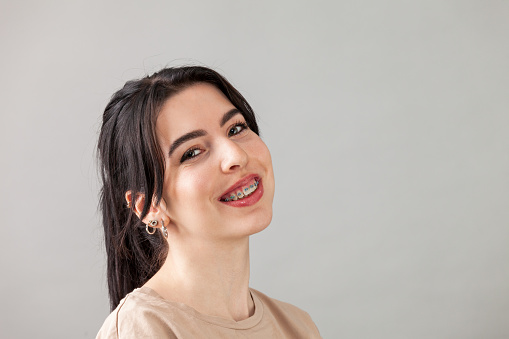 Close-up studio portrait of a cheerful 20 year old white woman with black hair in a beige t-shirt against a gray background