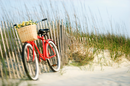 Red vintage bicycle with basket and flowers leaning on wooden fence at beach.