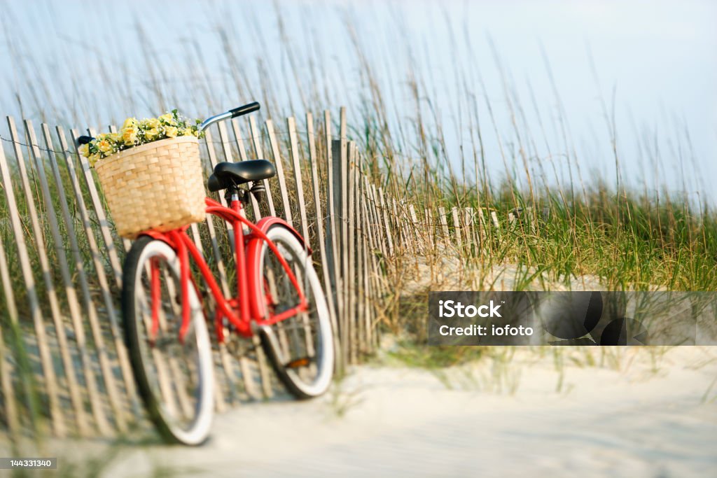 Bike by fence at beach. Red vintage bicycle with basket and flowers leaning on wooden fence at beach. Beach Stock Photo