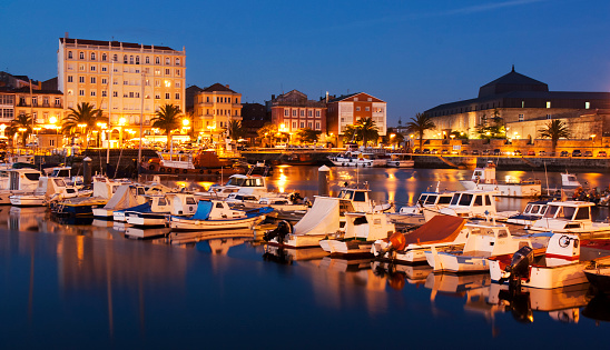 Long exposure night view of old harbor and townscape in Ferrol, A Coruña province, Galicia, Spain. Nautical vessels and fishing boats moored in a row.