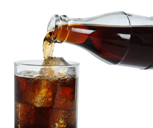 istock Pouring cola from bottle into glass with ice cubes on white background, closeup. Refreshing soda water 1443317242