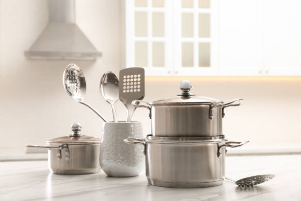 istock Set of stainless steel cookware and kitchen utensils on white table indoors 1443317347
