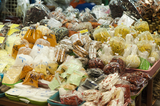Close-up of market stall with herbs and alternative medicine of local market in Bangkok Saphan Mai. A lot of different herbs and bags with pills and powders are stacked in baskets