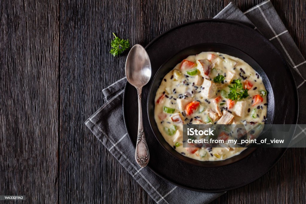 Turkey Wild Rice Soup in bowl, top view Turkey Wild Rice Soup with red potatoes. carrot, celery, spices and herbs in black bowl on dark wooden table with spoon, horizontal view from above, flat lay, free space Soup Stock Photo