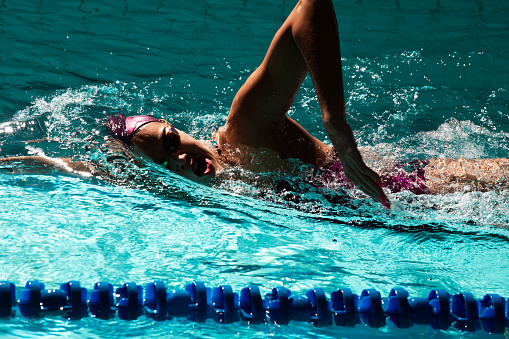 Female athlete in action, performing the backstroke swim technique in the indoor lap pool. Competitive back crawl stroke concept.